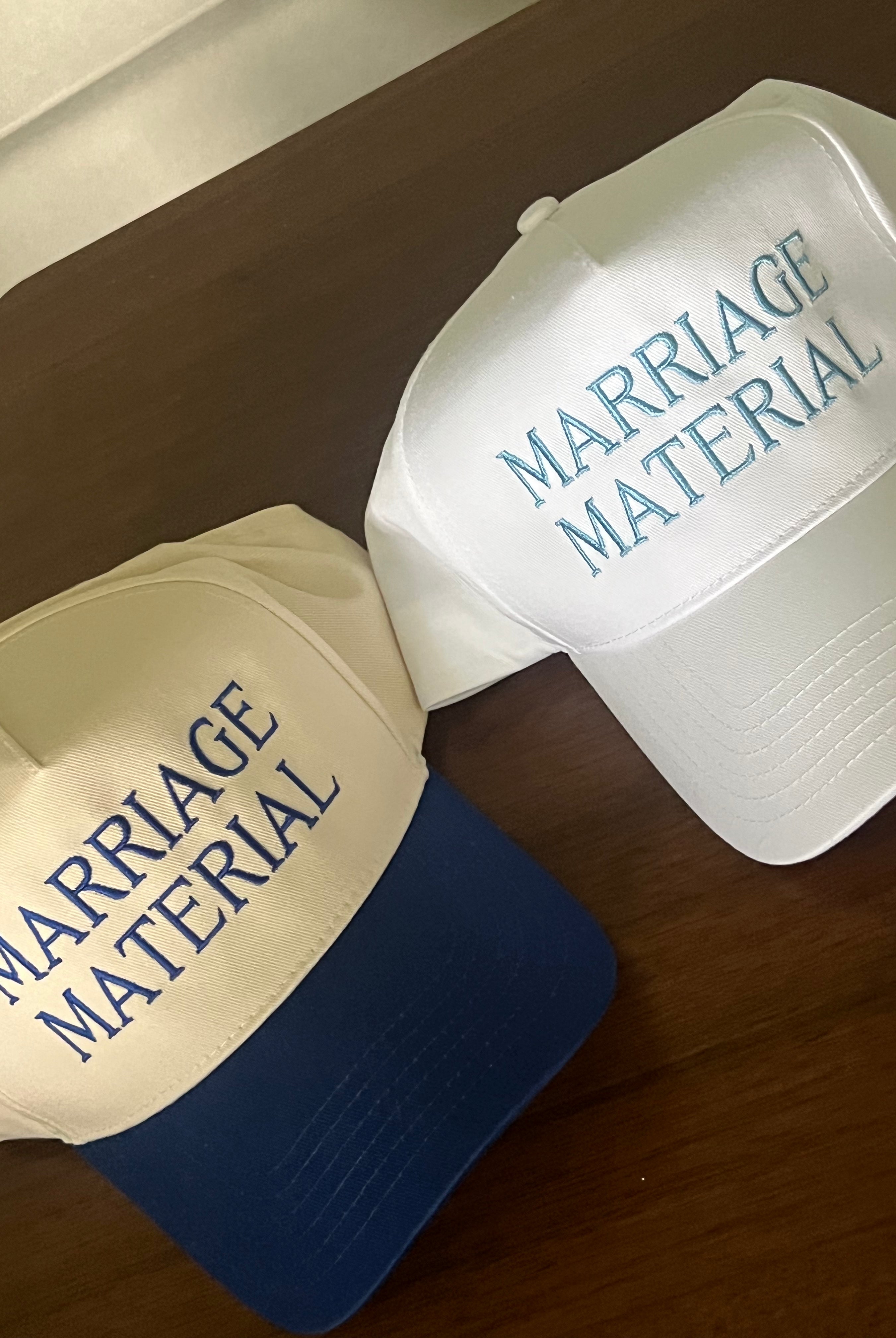 Two hats with 'Marriage Material' text on a wooden surface