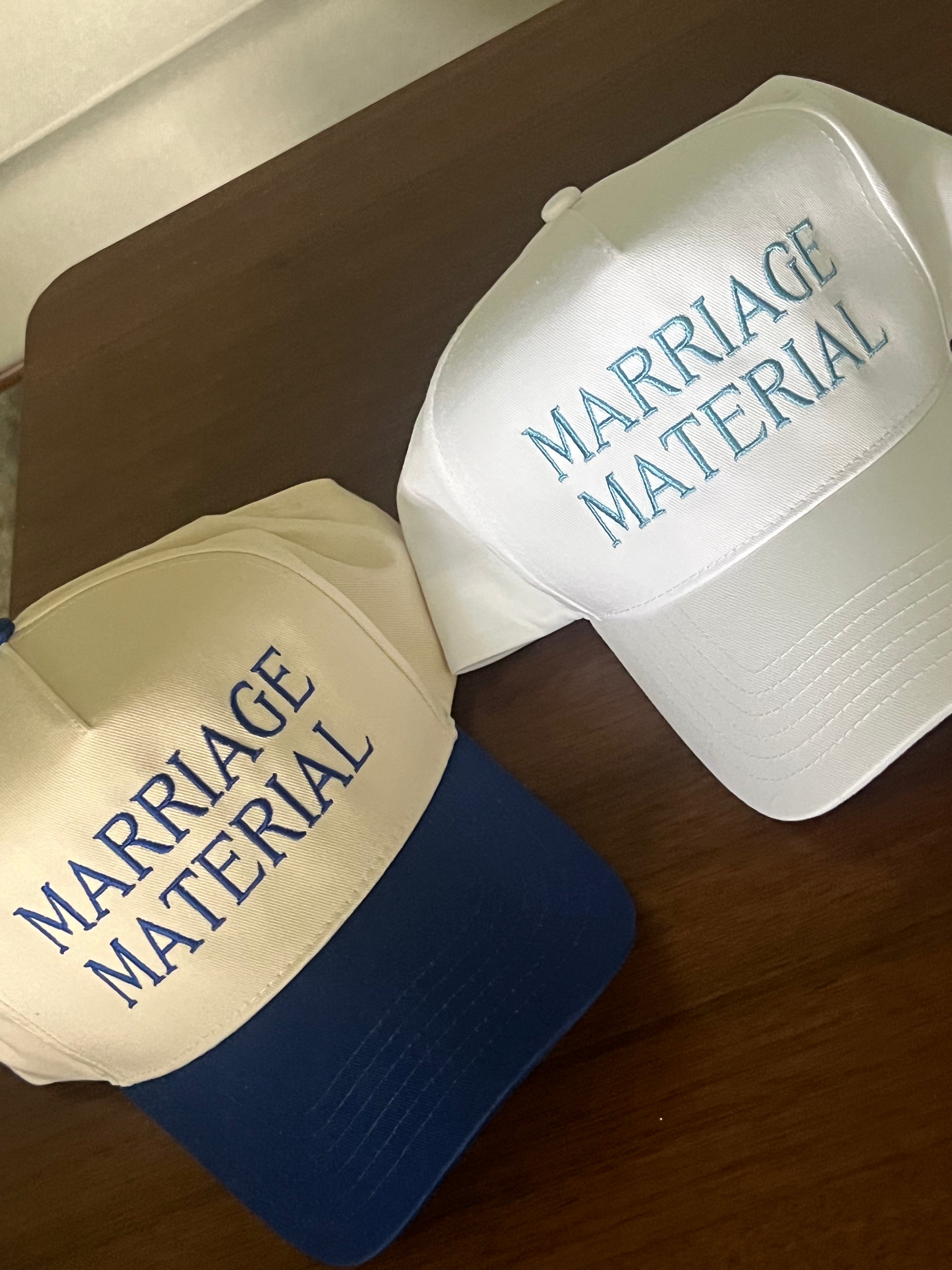 Two hats with 'Marriage Material' text on a wooden surface