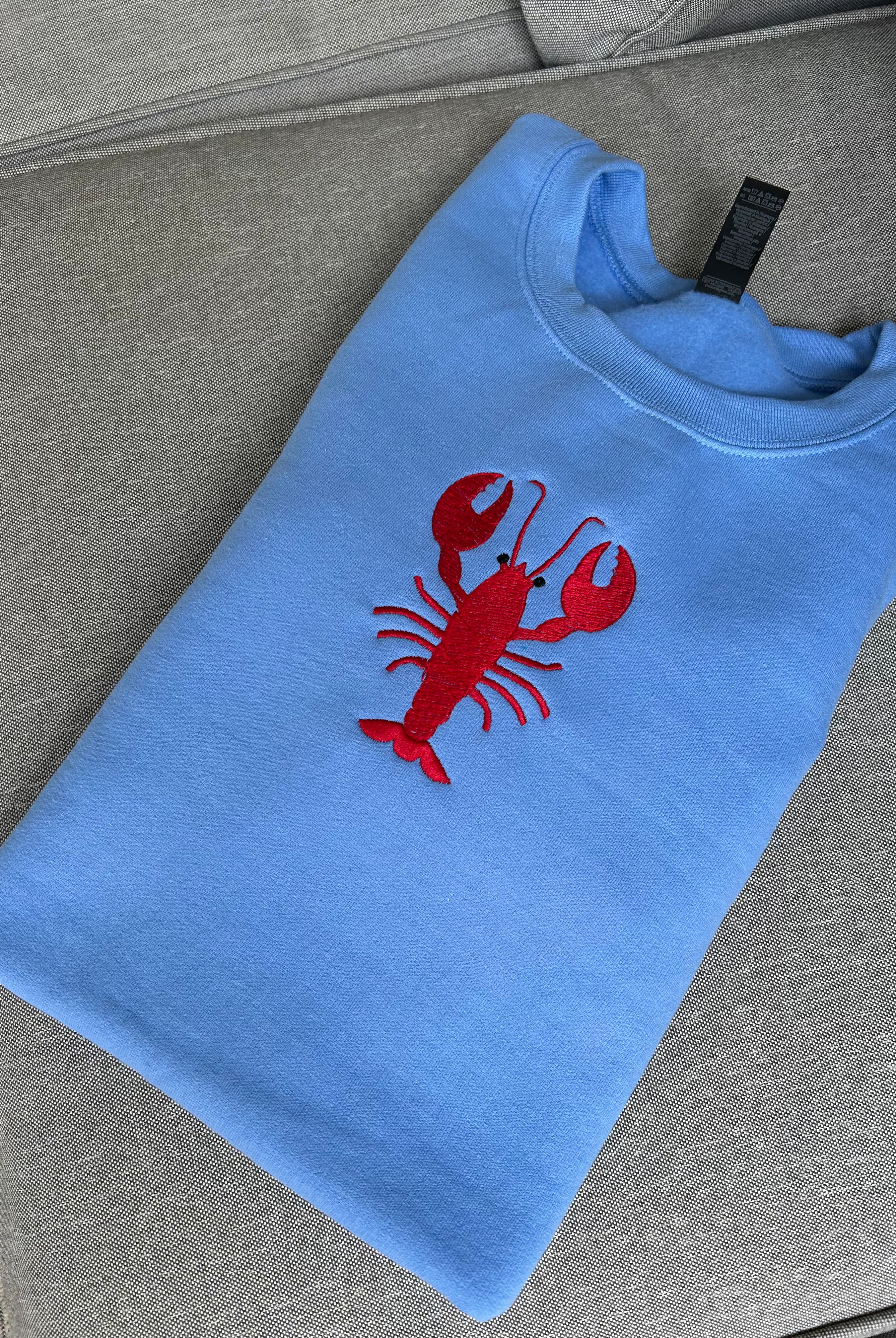 Blue embroidered sweatshirt with a red lobster design on a gray surface