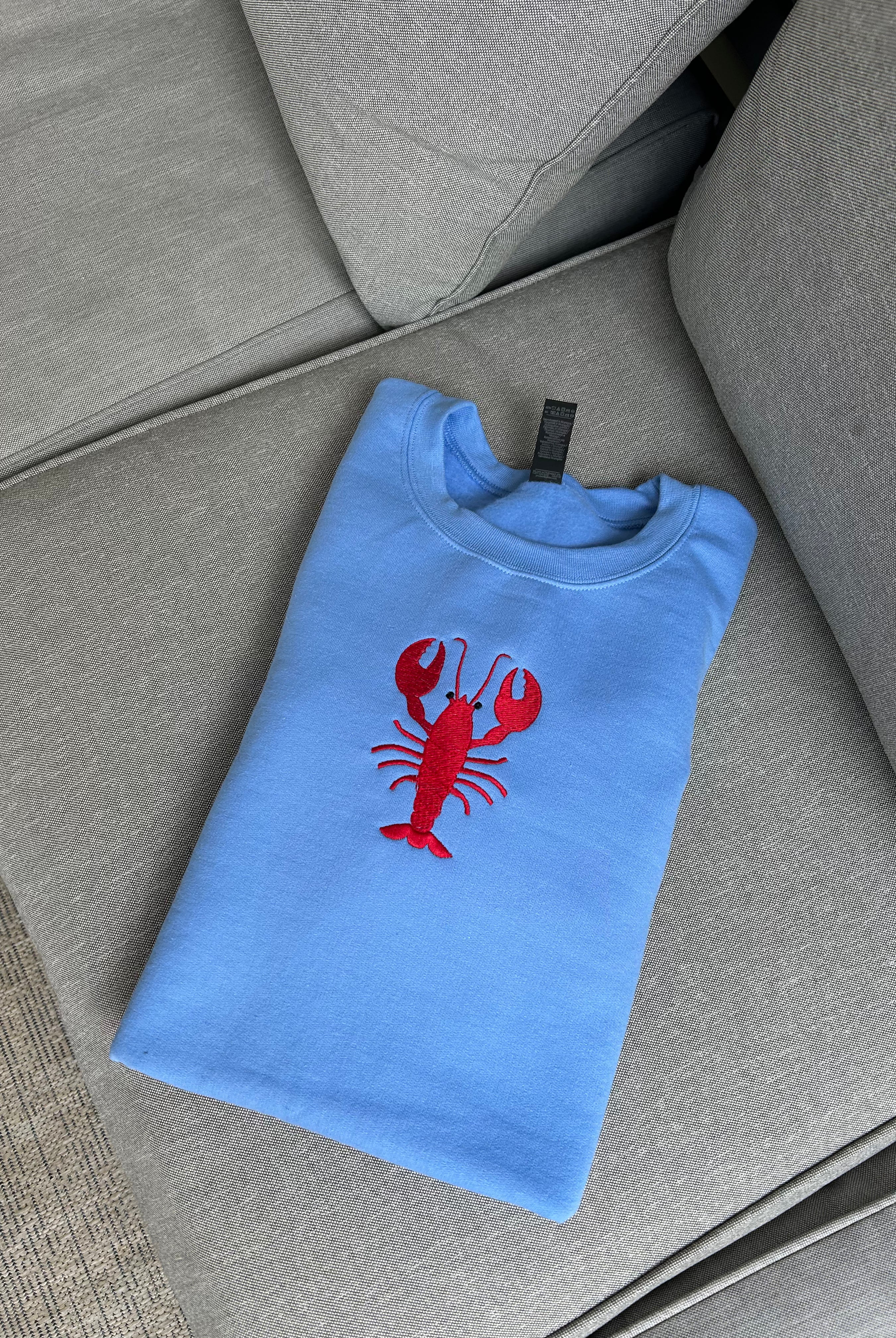 Folded blue t-shirt with a red lobster design on a gray surface