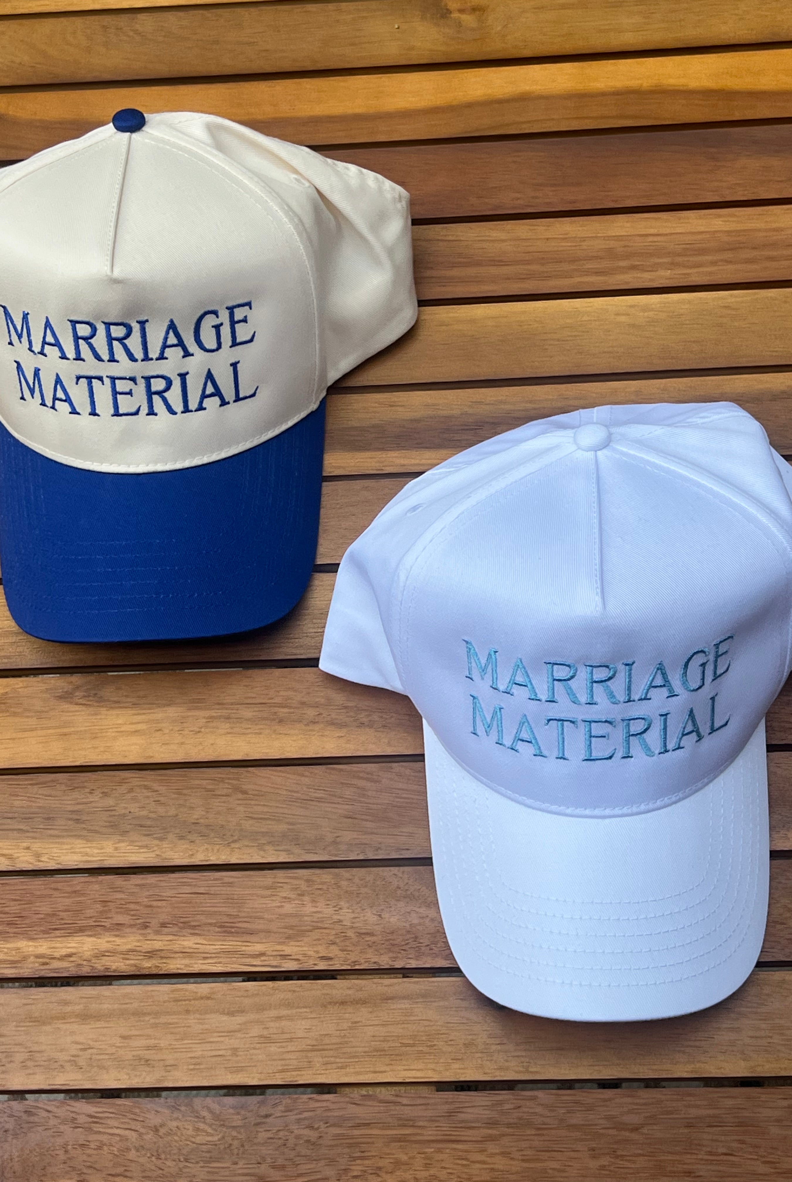 Two hats with 'MARRIAGE MATERIAL' text on a wooden surface