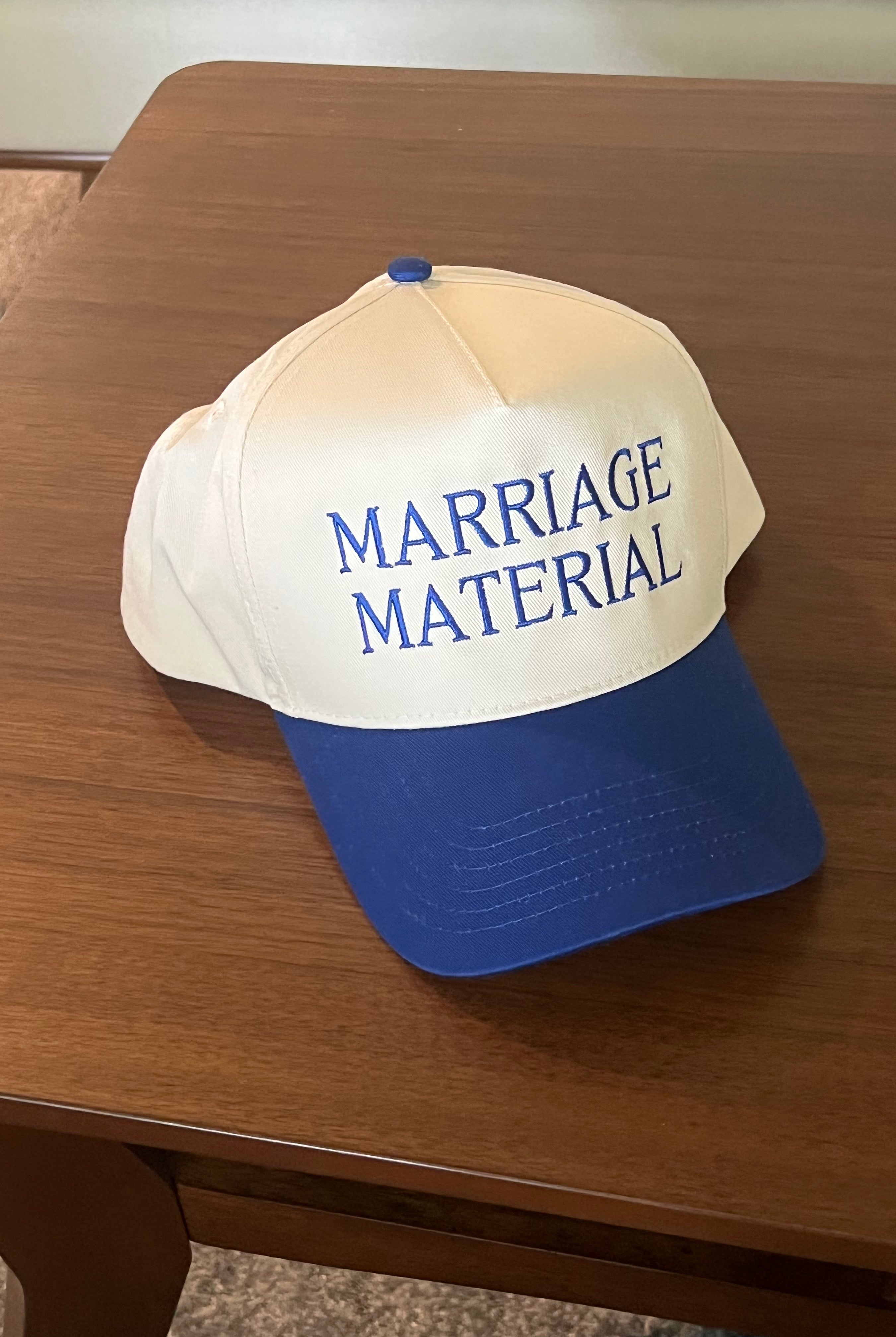 Cap with 'MARRIAGE MATERIAL' text on a wooden surface