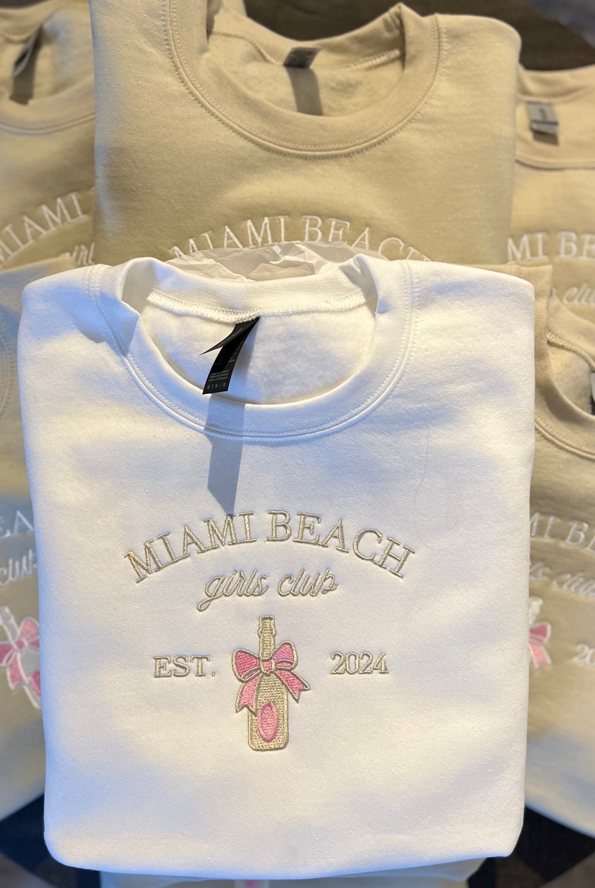 A collection of custom embroidered sweatshirts with various texts and designs in neutral colors