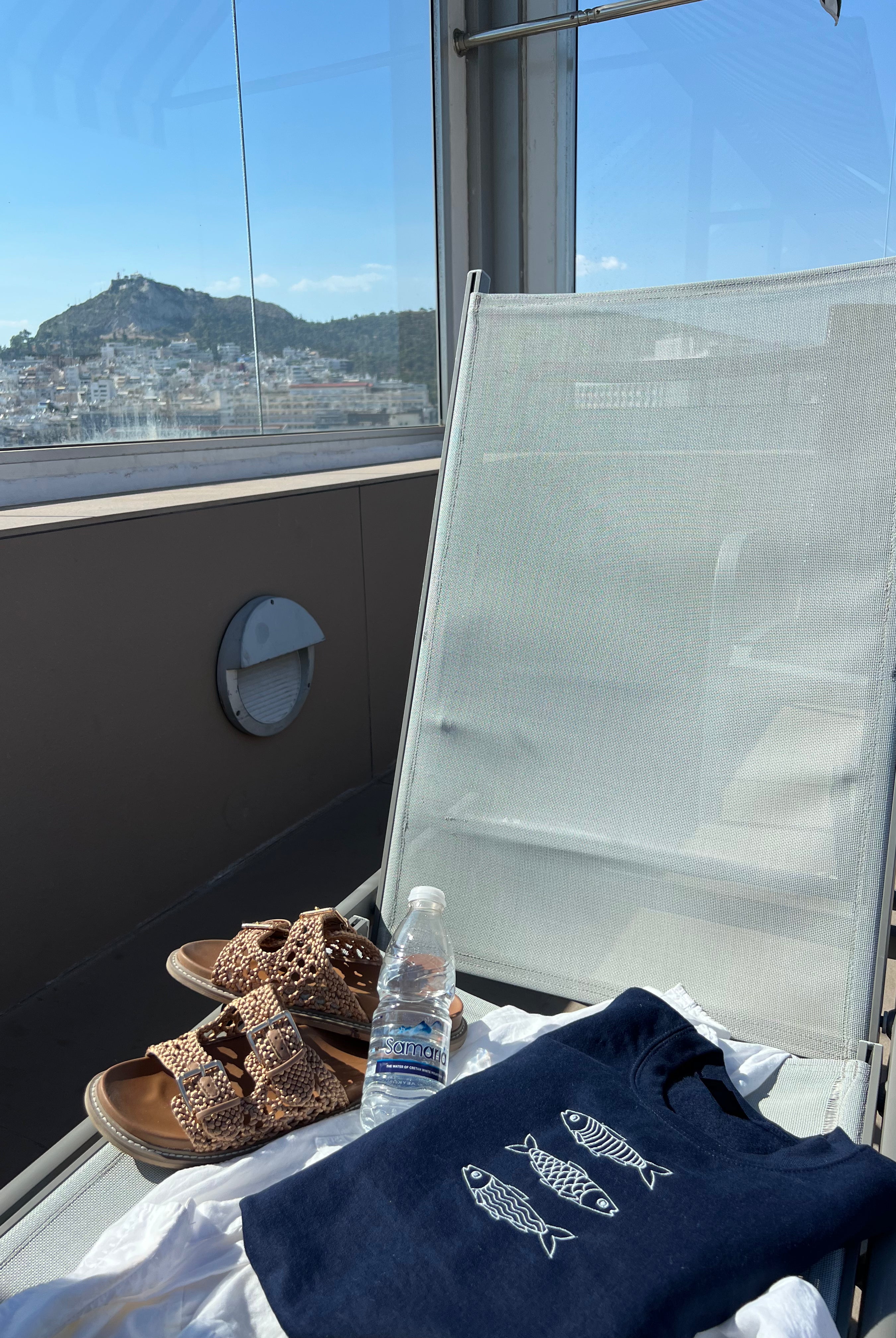 Navy blue sweatshirt with white design, sandals, and water bottle on a white chair with a scenic view in the background.