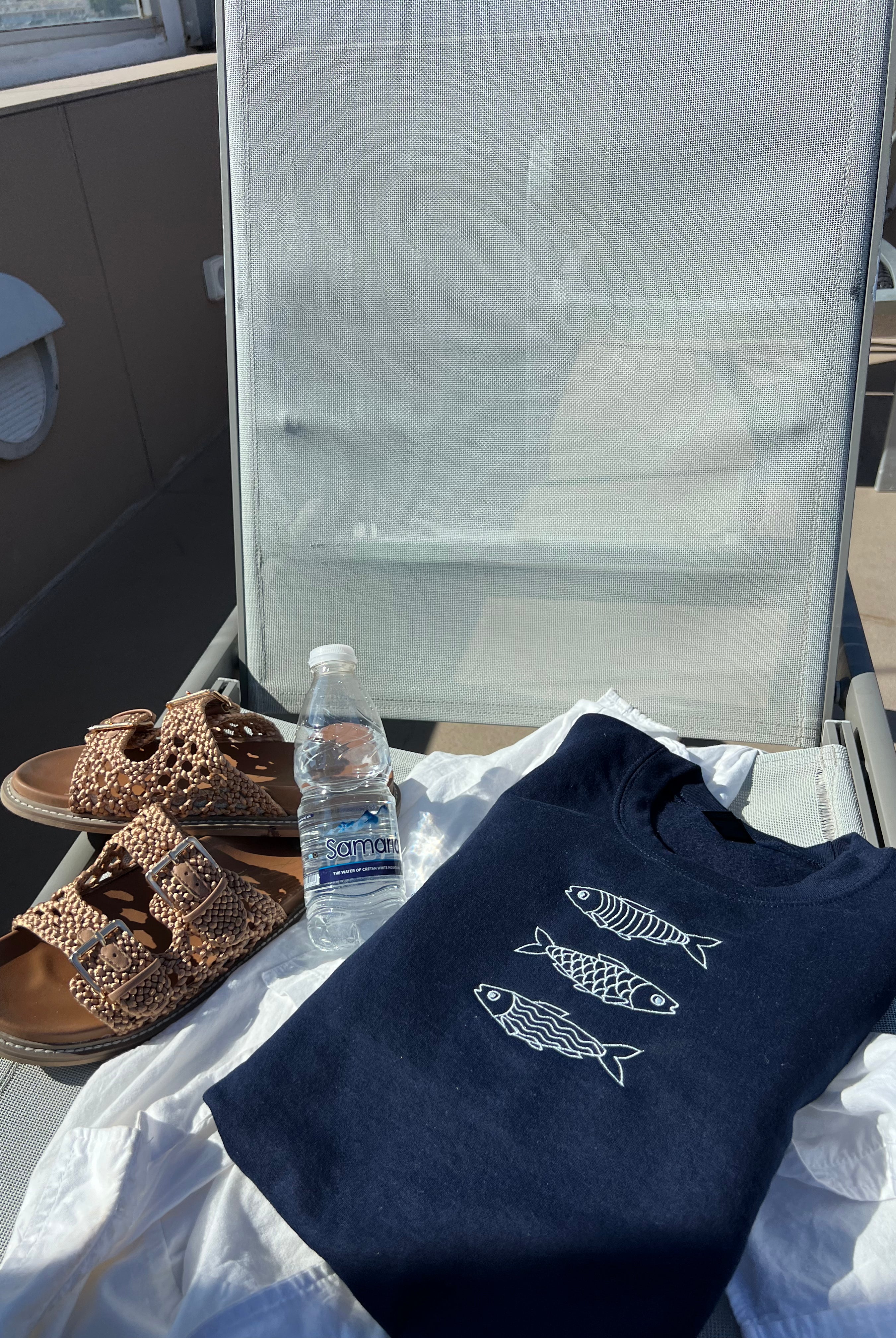Navy blue sweatshirt with fish designs, sandals, and a water bottle on a chair outdoors.