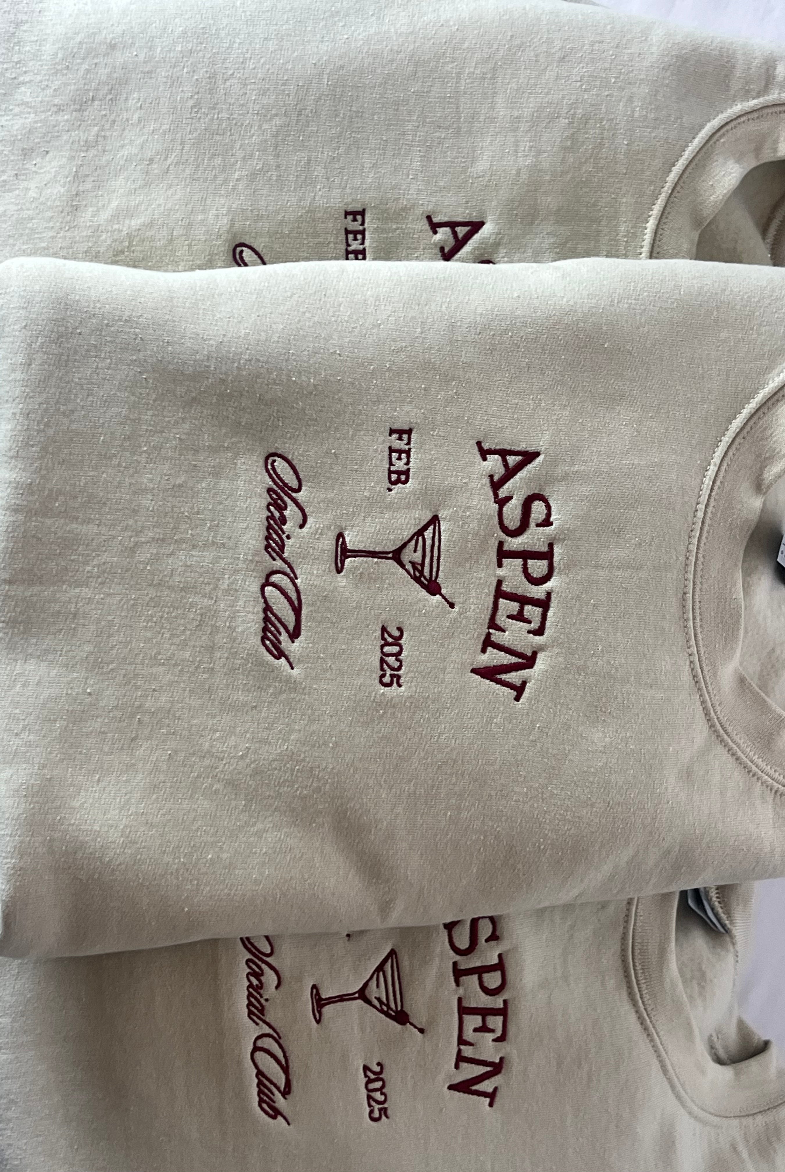 A collection of embroidered sweatshirts with 'ASPEN' text embroidered on them, displayed in a stacked arrangement.