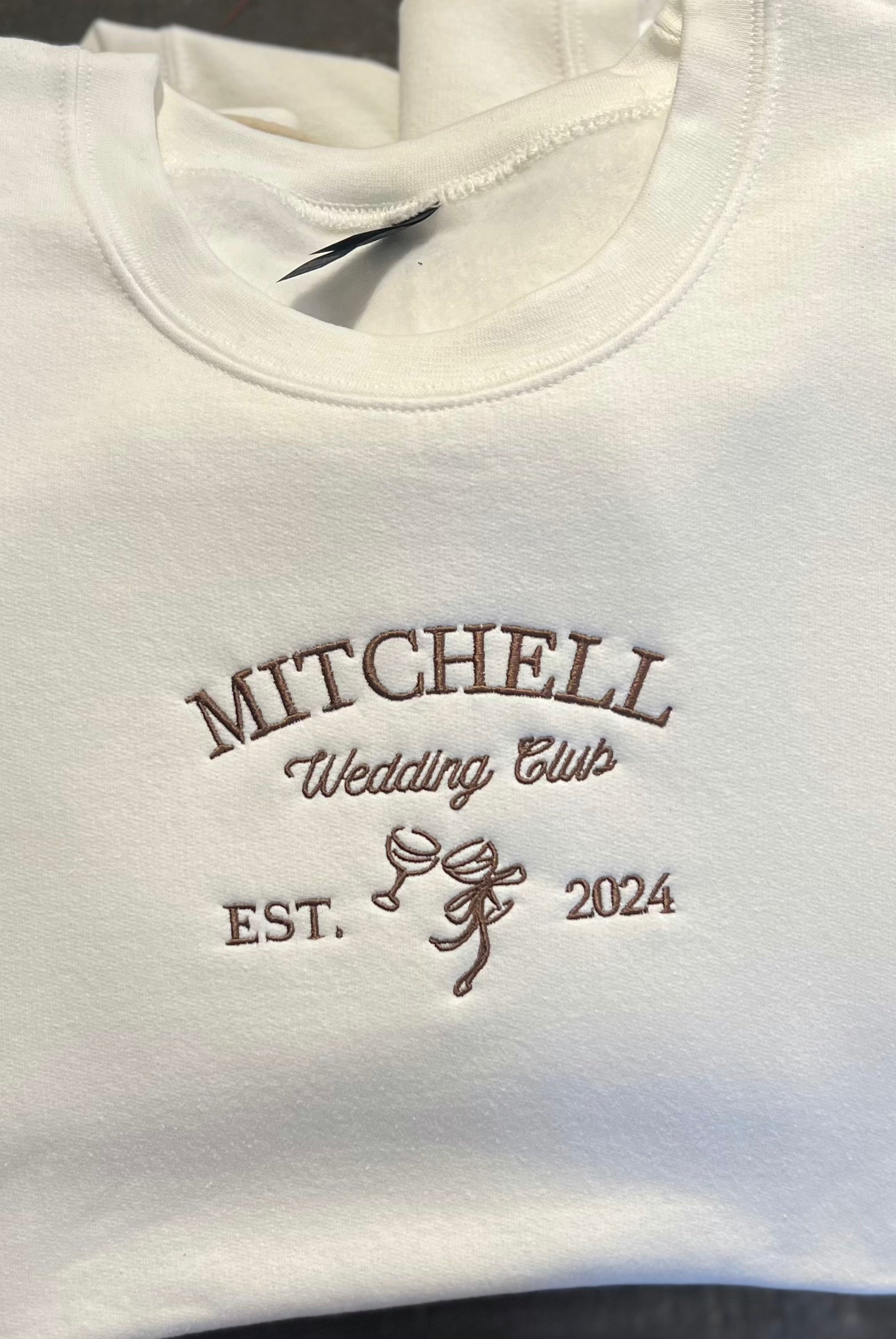 A collection of white embroidered sweatshirts with the text 'MITCHELL Wedding Club EST. 2024' on them.