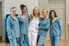 A group of people wearing matching embroidered zip-up jackets in a light color.