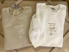 Two folded embroidered crewneck sweatshirts, one beige and one white, with a custom margarita glass design and text on them.