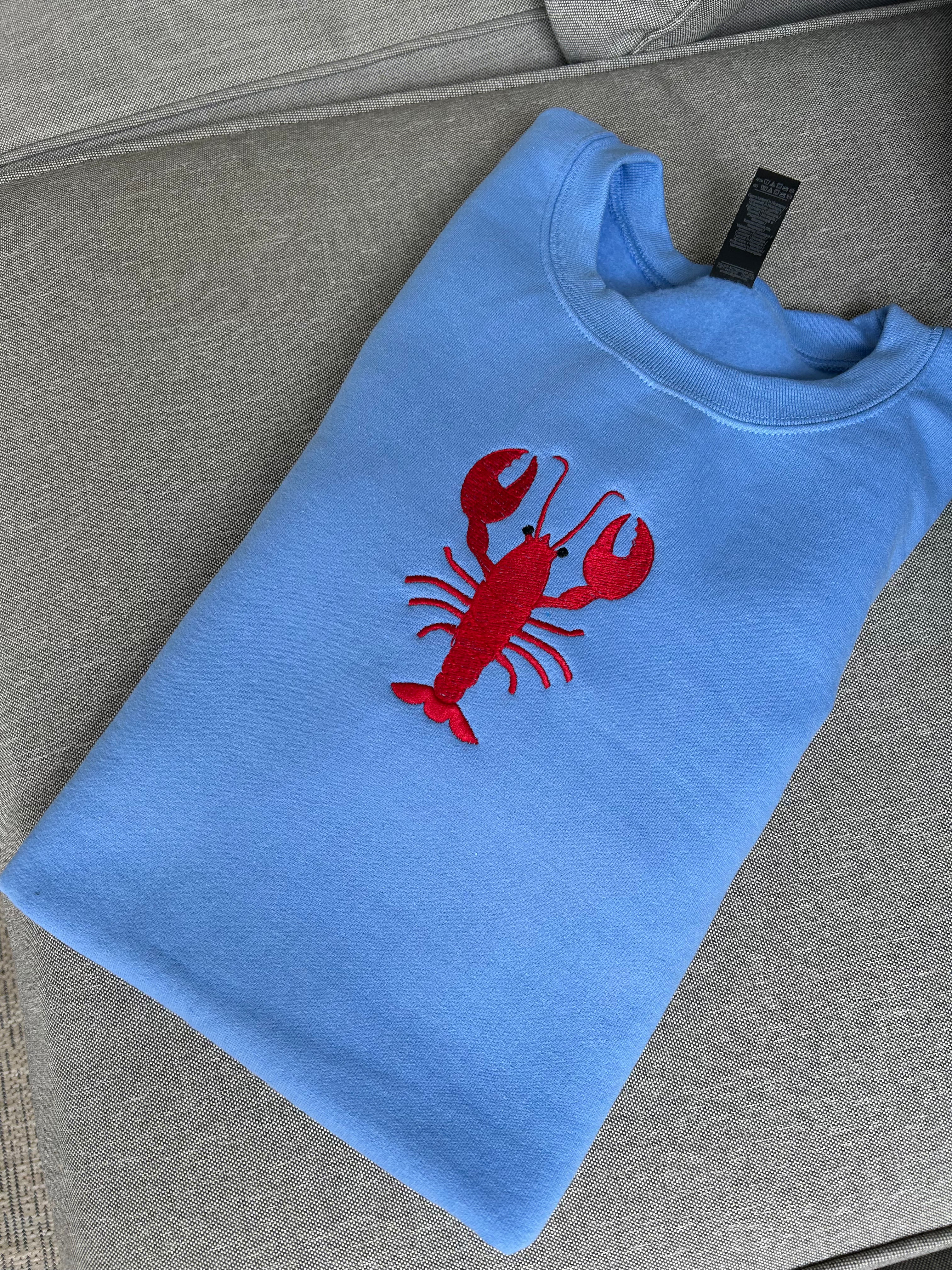 Blue embroidered sweatshirt with a red lobster design on a gray surface