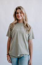 A person wearing a green t-shirt with 'God is Good' embroidered on the front.