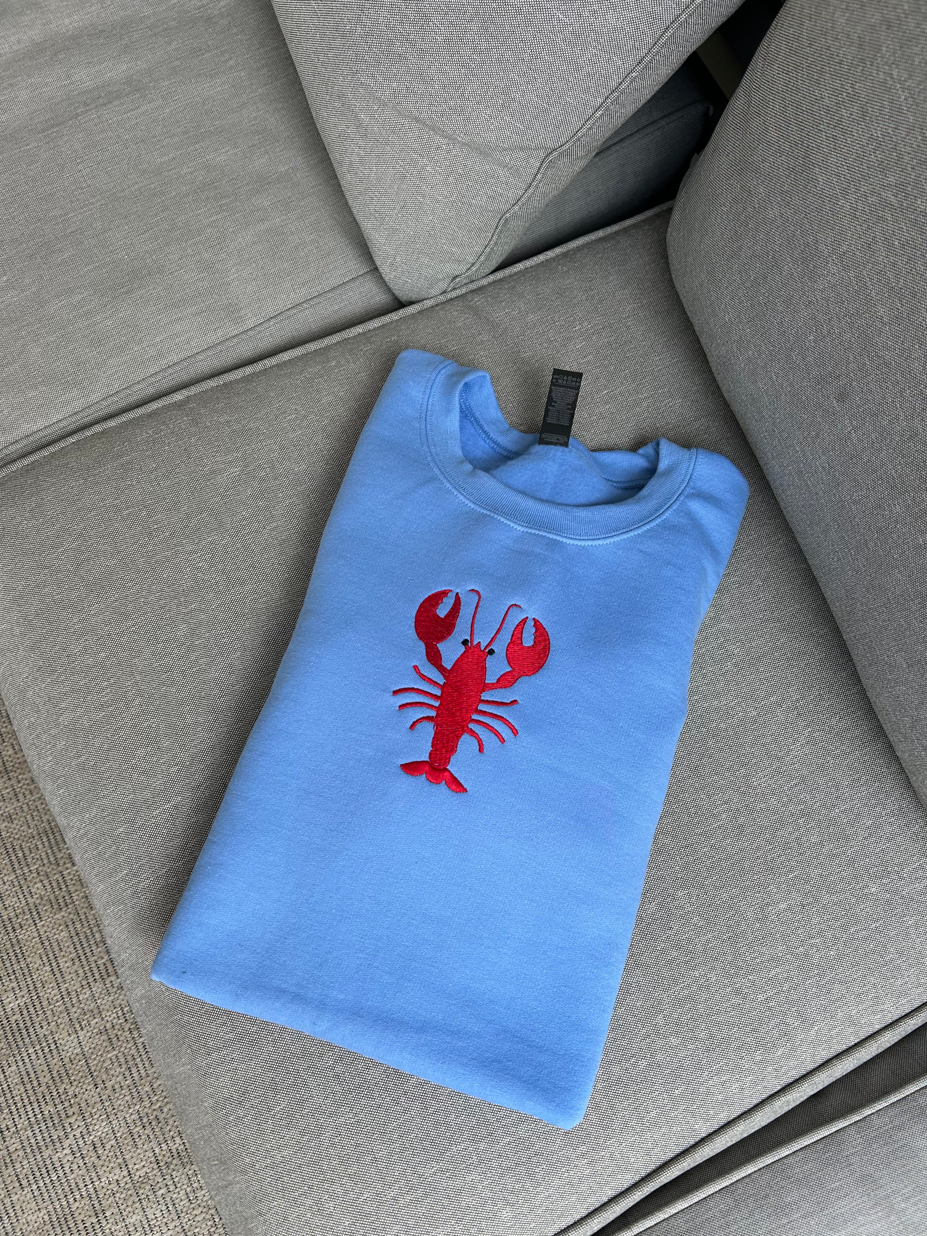 Folded blue t-shirt with a red lobster design on a gray surface