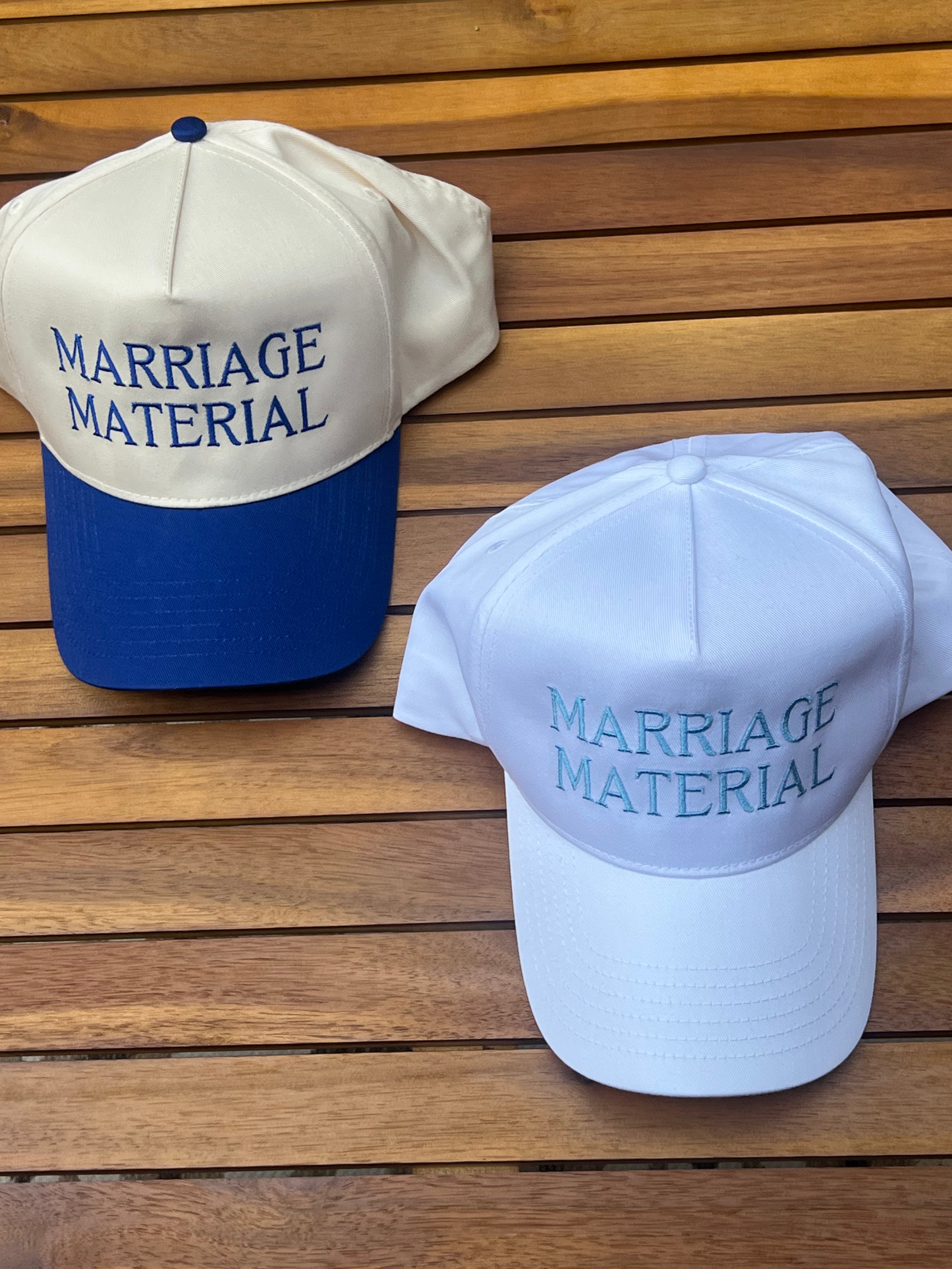 Two hats with 'MARRIAGE MATERIAL' text on a wooden surface