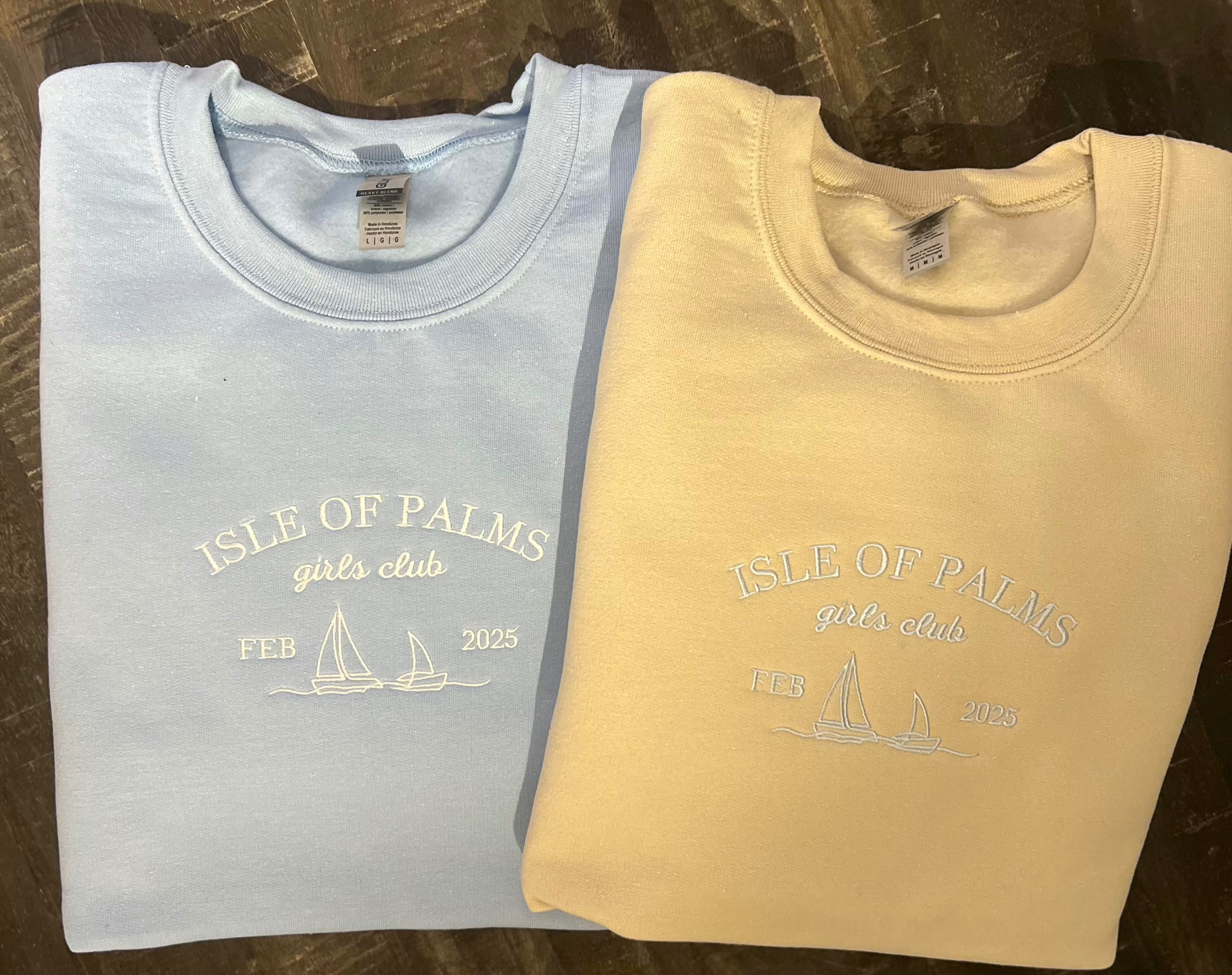 Two crewneck sweatshirts, one in blue and one in a beige color, each with a embroidered sailboat design and the text 'ISLE OF PALMS YACHT CLUB'.