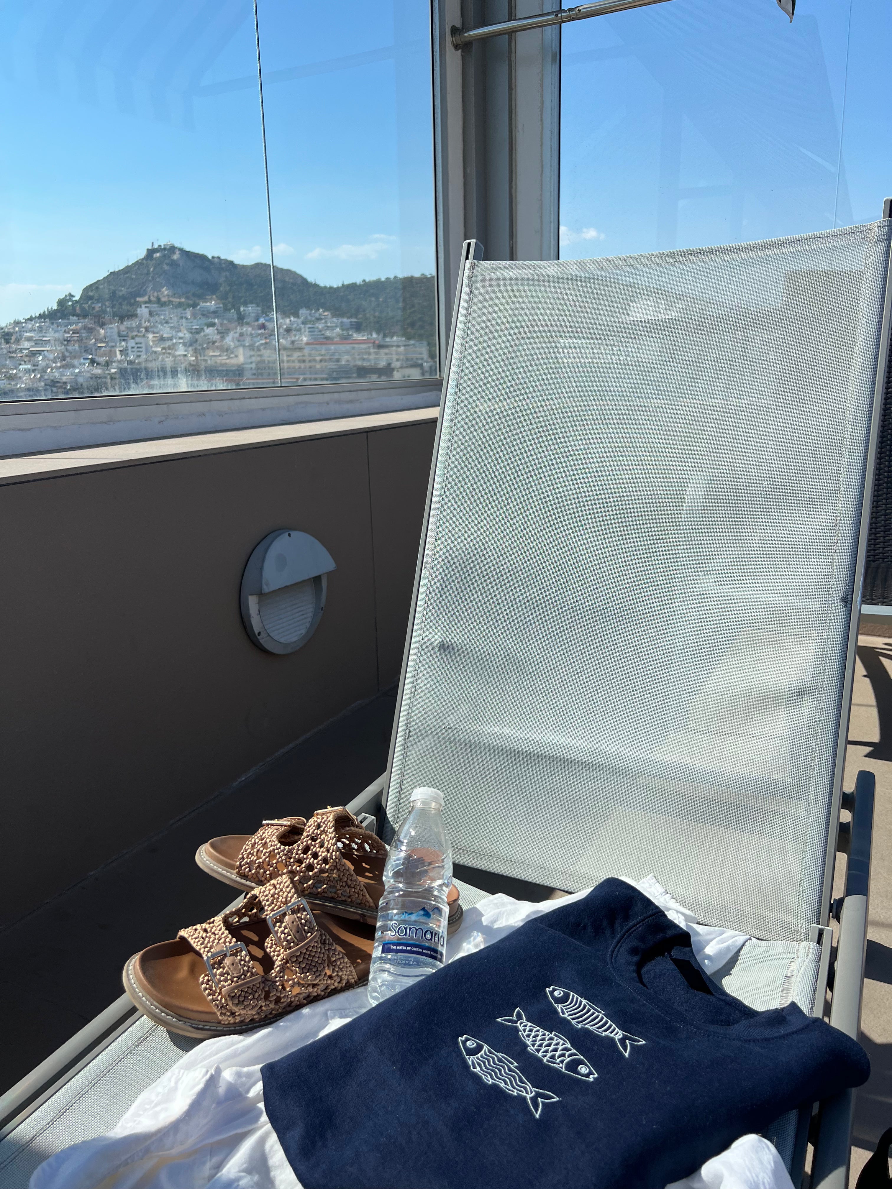 Navy blue sweatshirt with white design, sandals, and water bottle on a white chair with a scenic view in the background.
