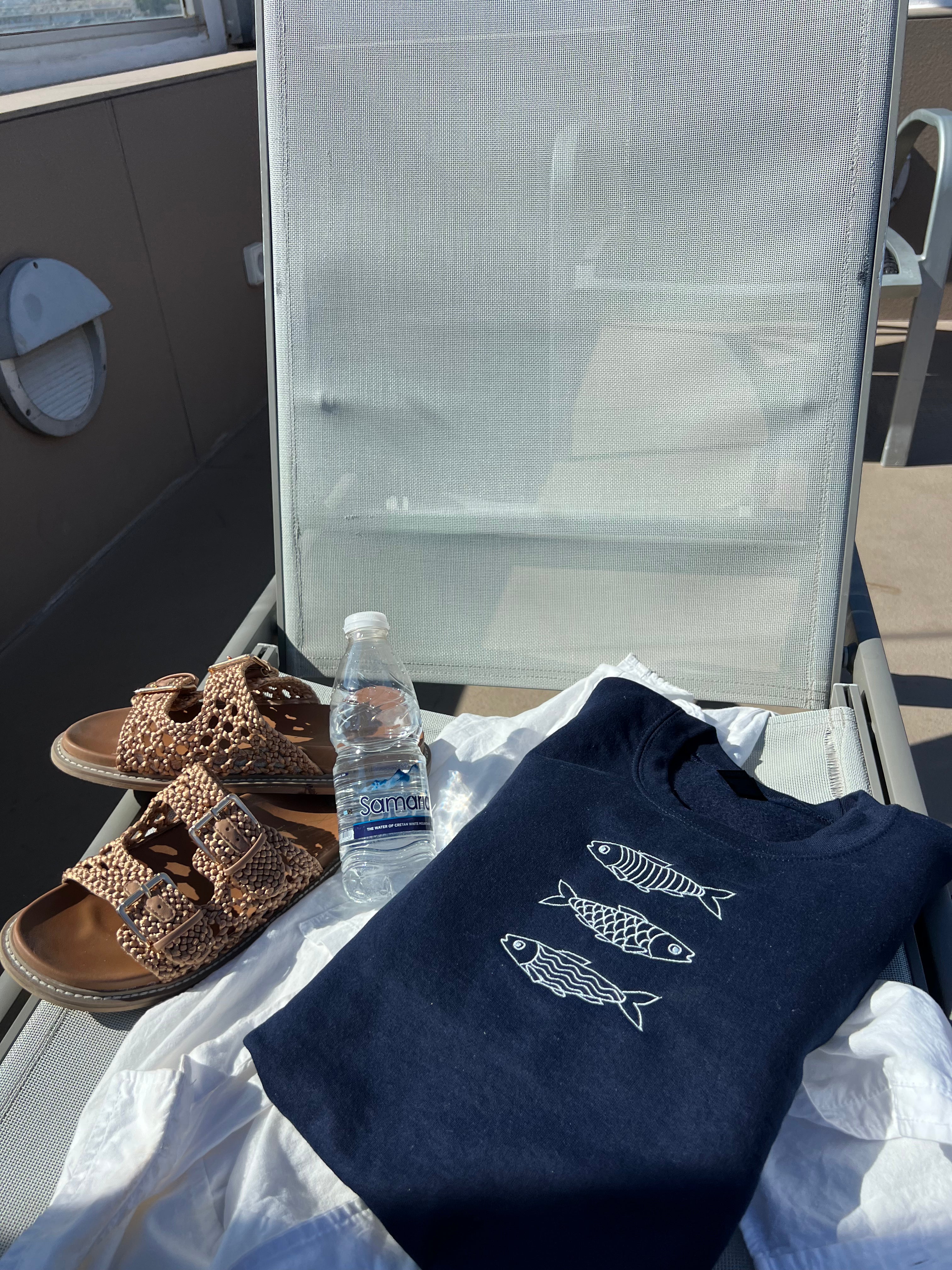 Navy blue sweatshirt with fish designs, sandals, and a water bottle on a chair outdoors.