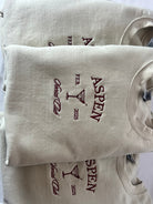 A collection of embroidered sweatshirts with 'ASPEN' text embroidered on them, displayed in a stacked arrangement.