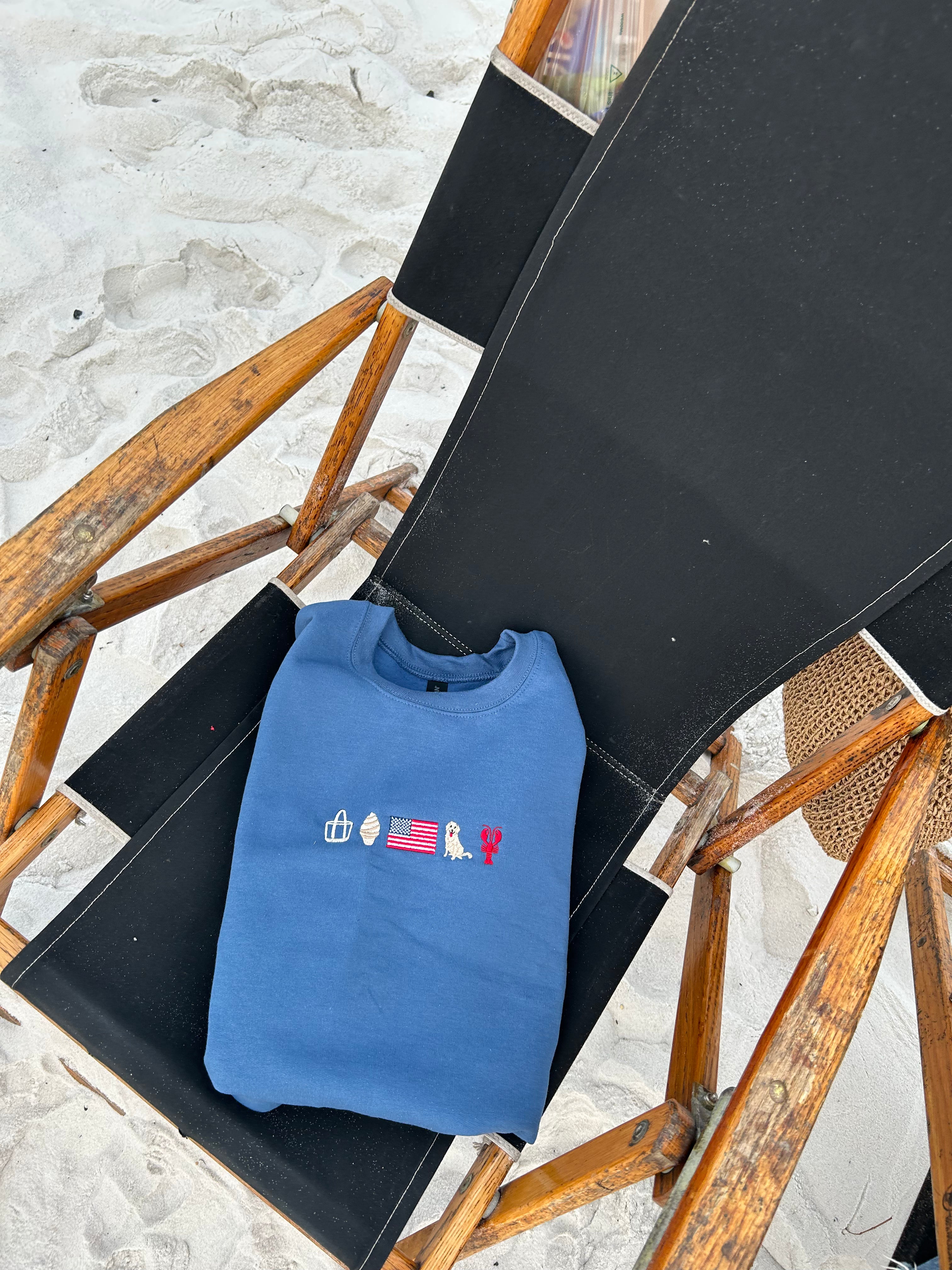 Blue sweatshirt with embroidered designs on a black chair on a sandy background